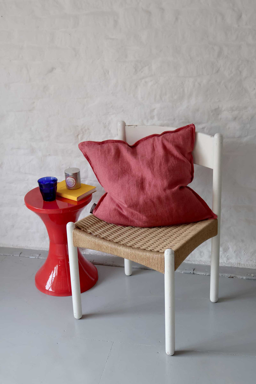 Red pillow on a white chair next to a red side table with a gray wall background