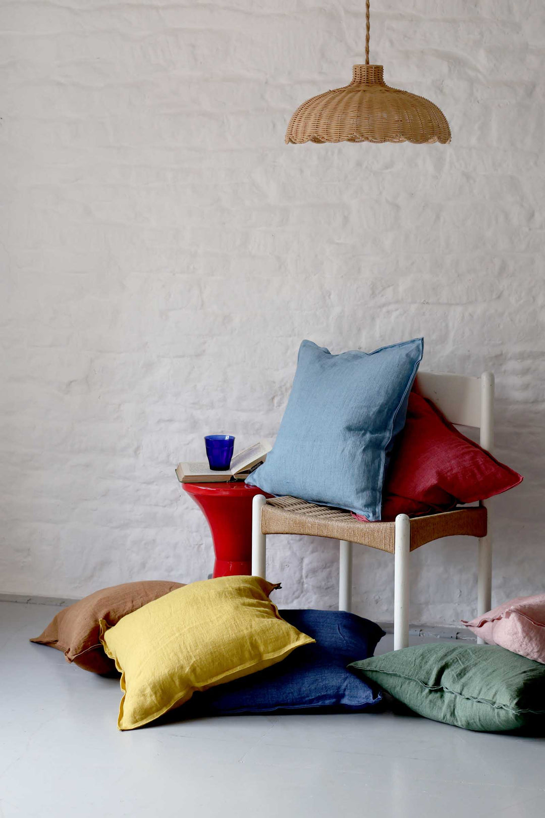 Colorful pillows on a chair against a white brick wall with a wicker lamp.