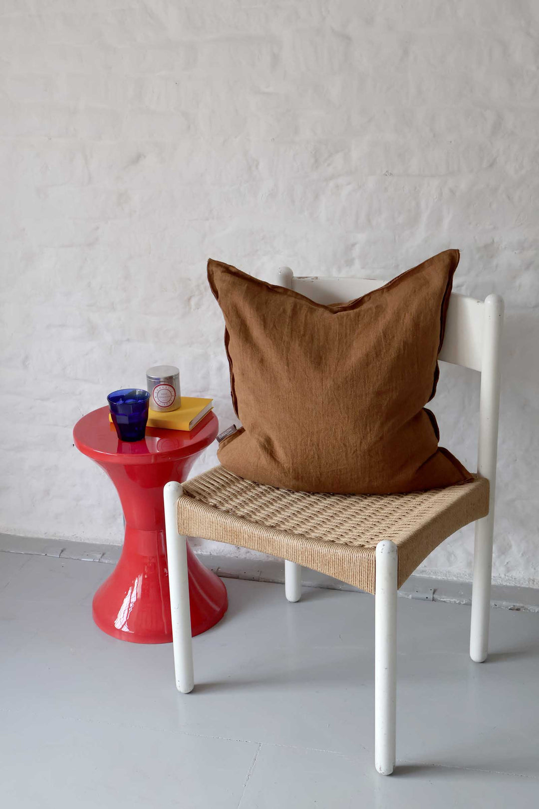 Chair with a brown pillow next to a red side table against a white wall.