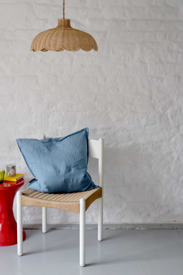 Blue pillow on a white chair against a textured white wall with a wicker lamp.