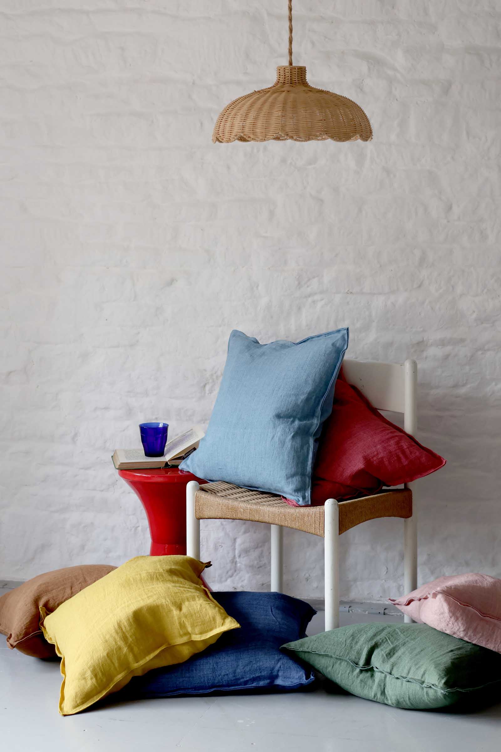 Colorful pillows on a chair against a white textured wall with a hanging lamp.