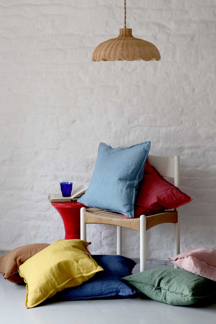 Colorful pillows on a chair against a white textured wall with a hanging lamp.