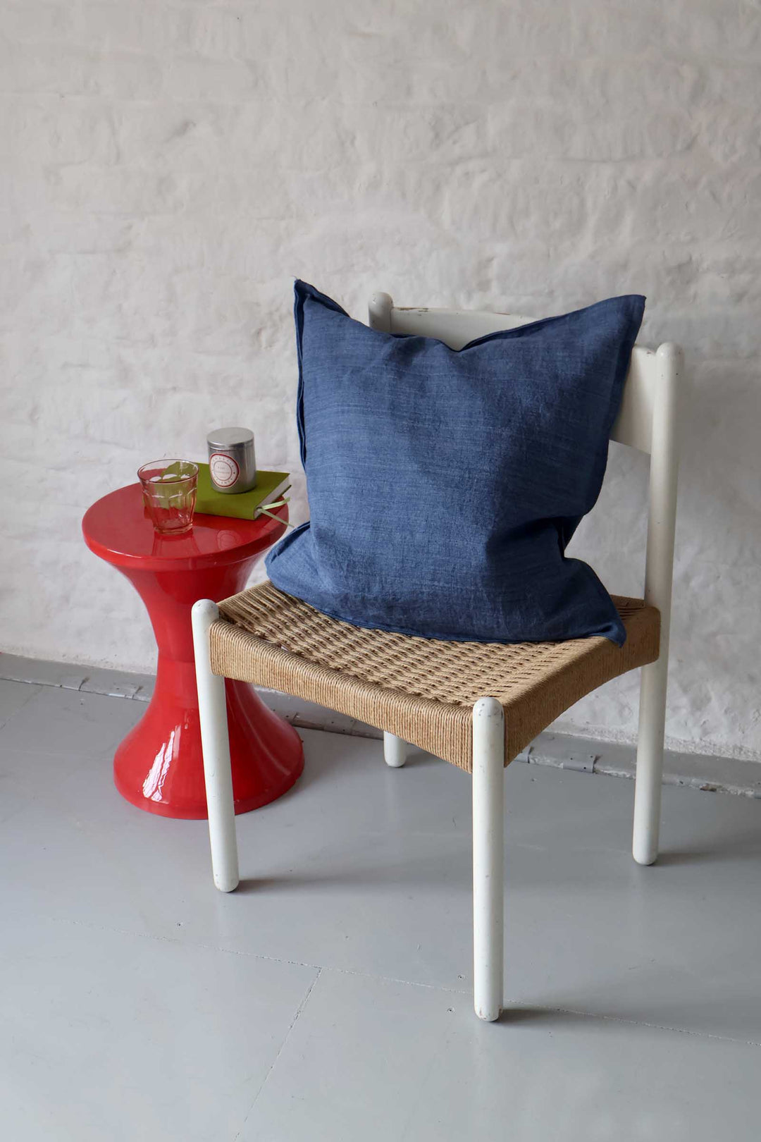 Chair with a blue cushion next to a red side table against a white wall.