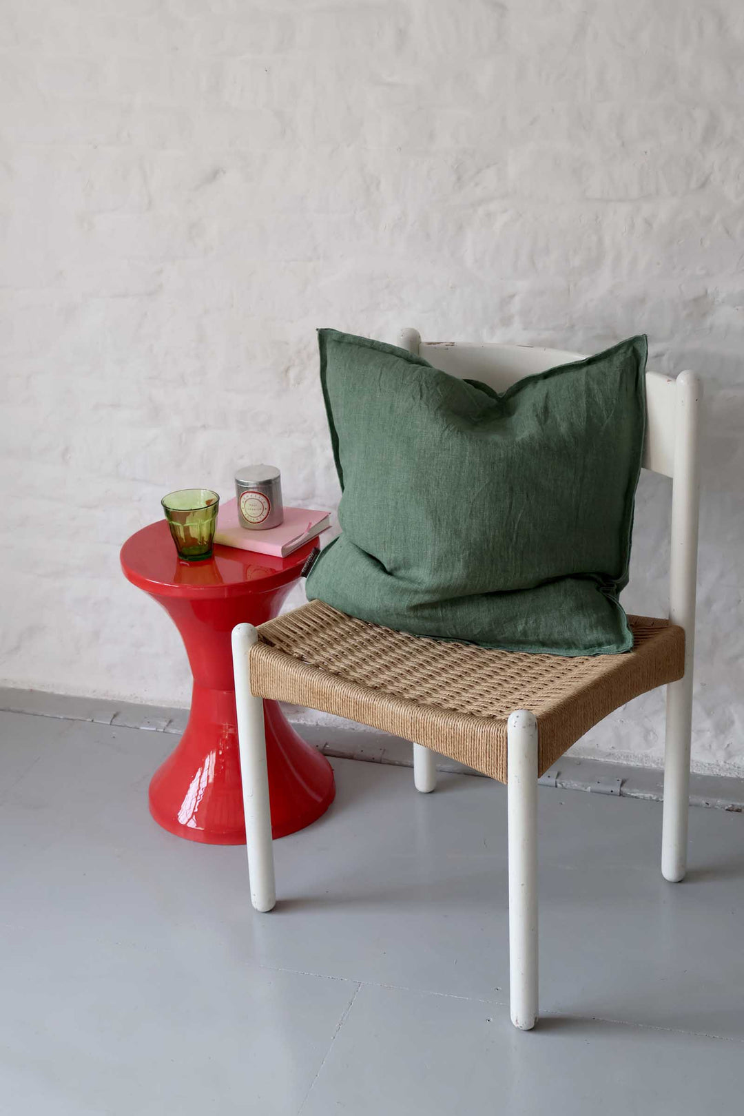 Chair with a green cushion and woven seat next to a red side table against a white wall.