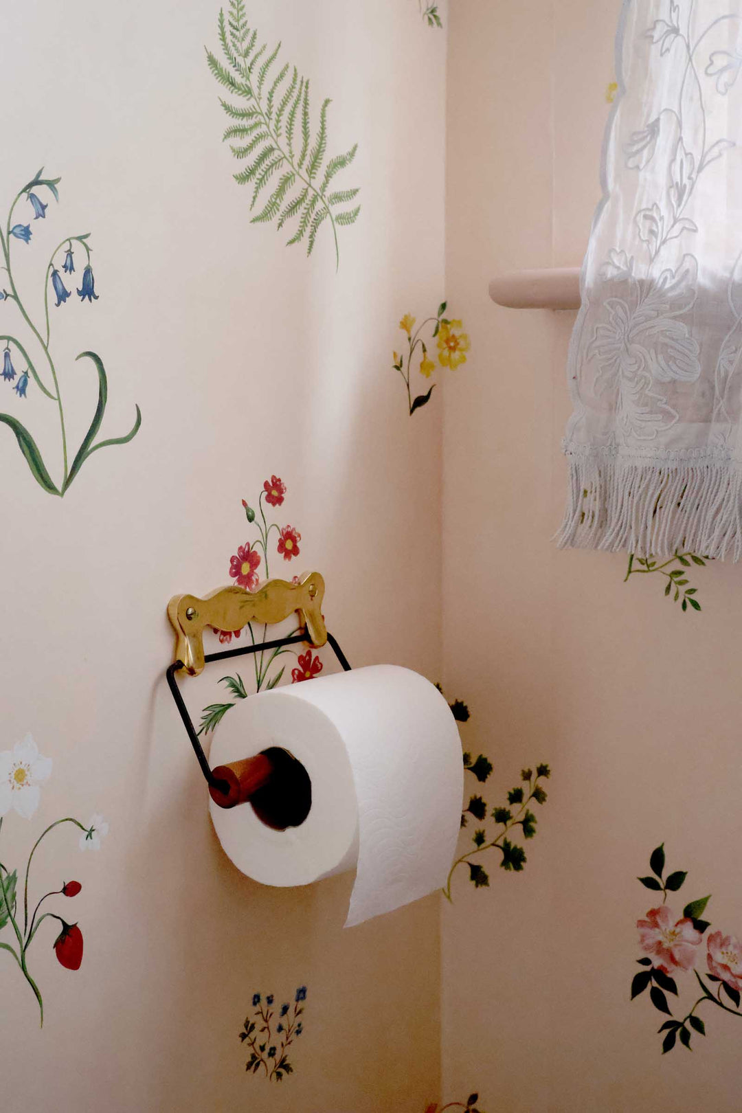 Toilet paper holder with a roll of toilet paper on a wall with floral designs.