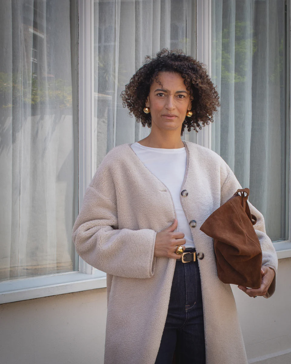 Woman holding a brown bag in front of a window with sheer curtains