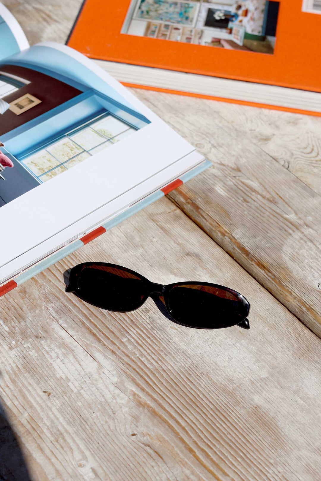 Black sunglasses on a wooden surface with an open book and orange object in the background