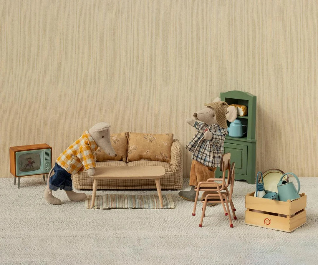 Miniature living room scene with toy furniture and figures on a neutral background