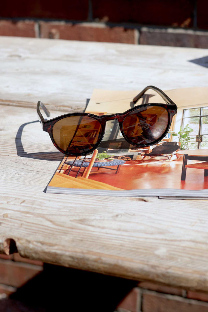 Sunglasses on a magazine with a beach scene cover on a wooden surface