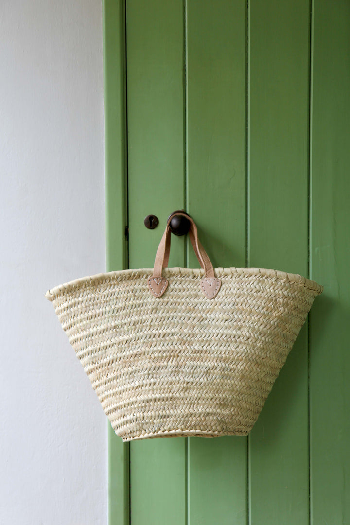 Woven basket with leather handles hanging on a green door.