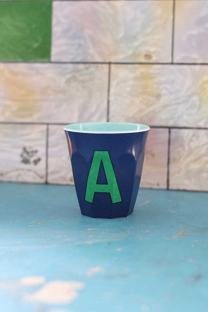 Blue cup with a green letter 'A' on a blue surface with a tiled wall background