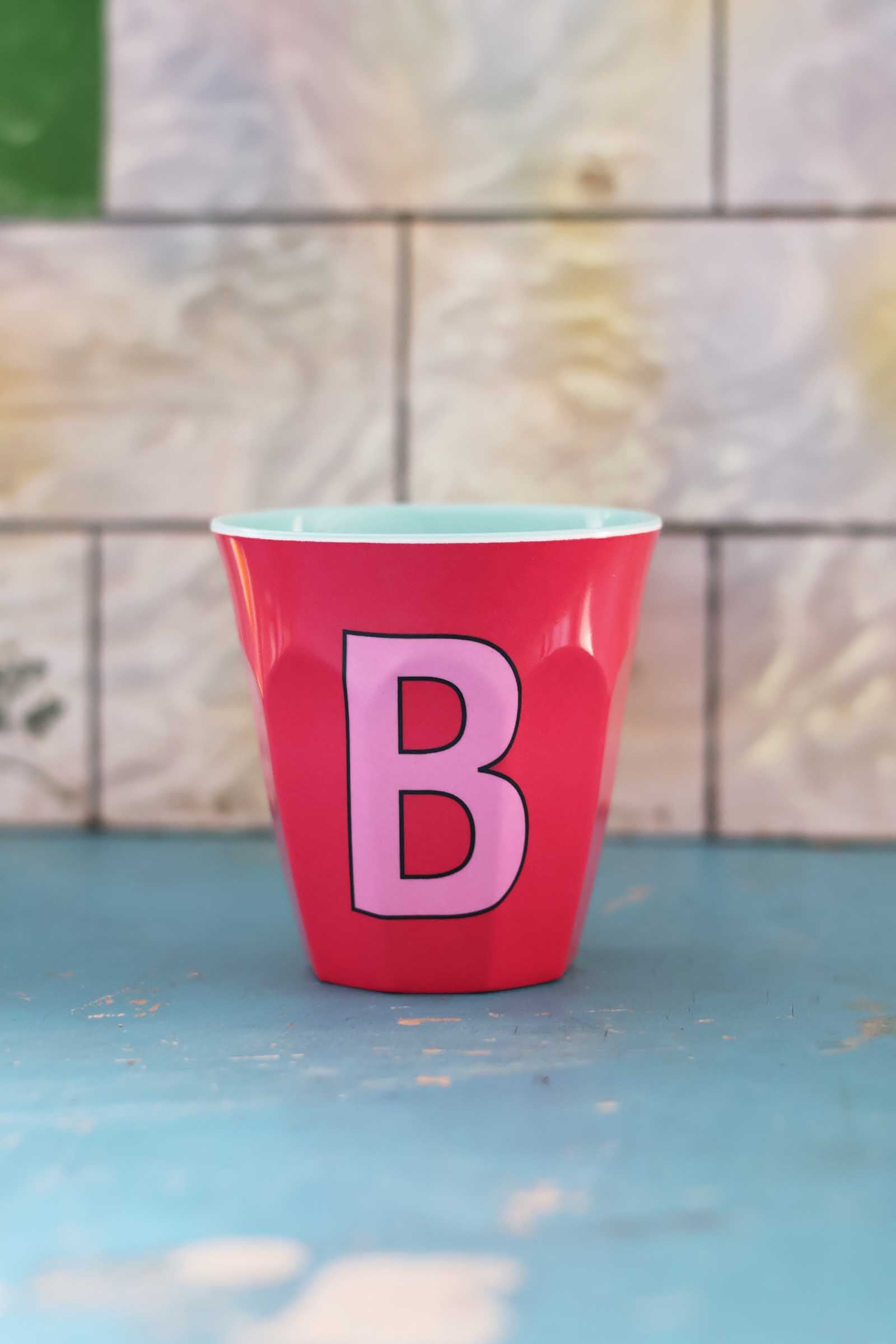 Red cup with a pink letter 'B' on a blue surface and tiled wall background