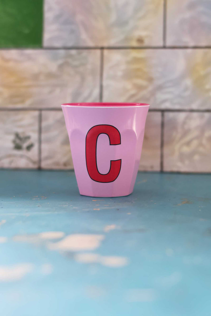 Pink cup with a red letter 'C' on a blue surface with a tiled background