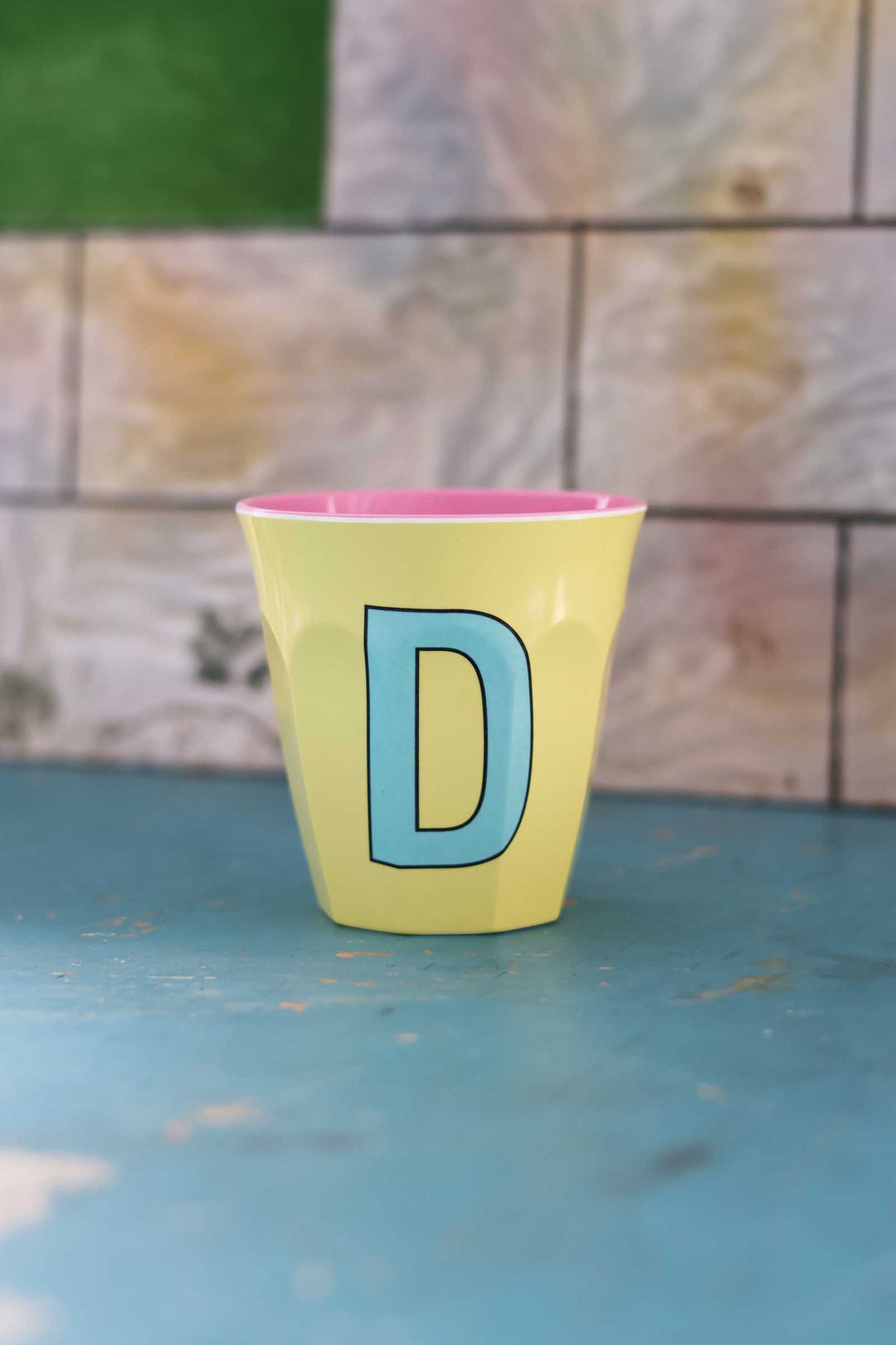 Yellow cup with a blue letter 'D' on a blue surface