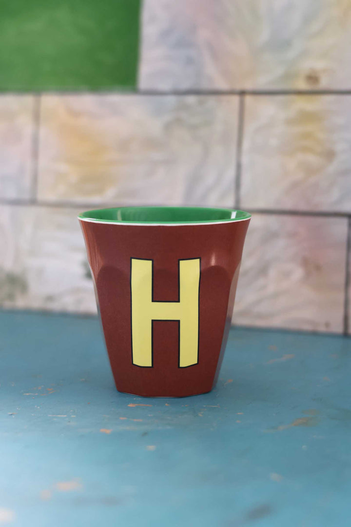 Red cup with a yellow 'H' on a blue surface and stone wall background
