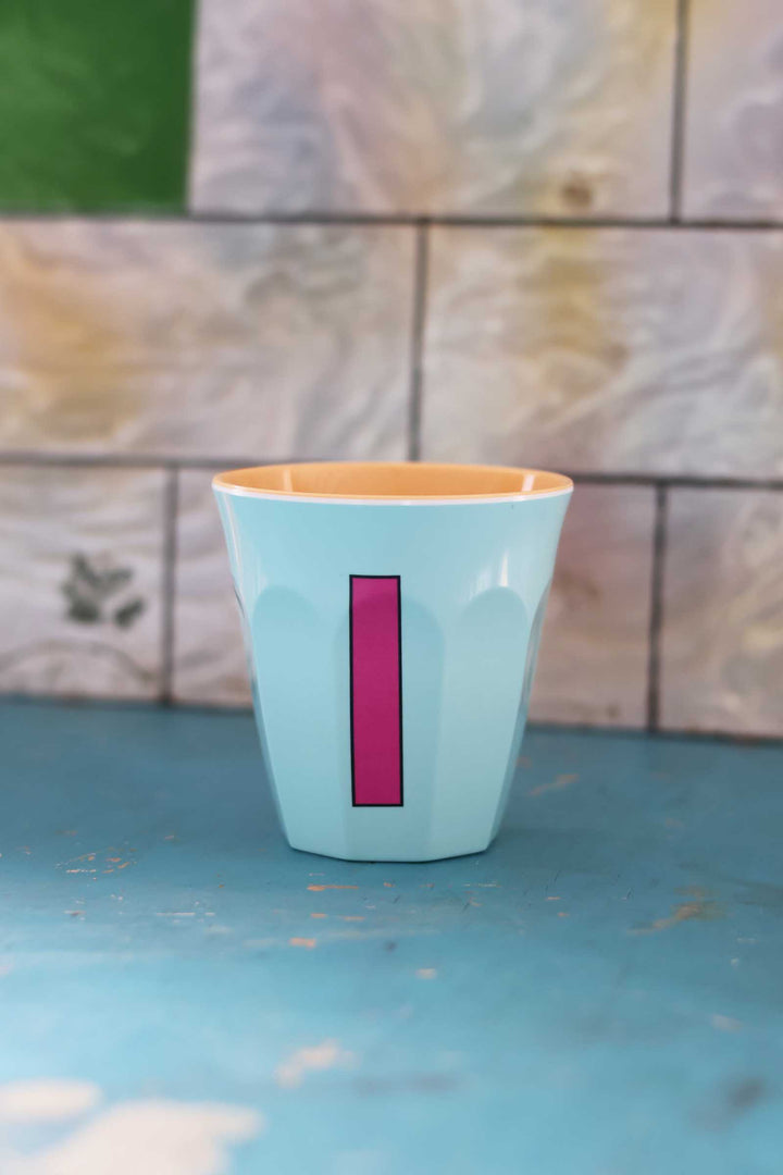 Light blue ceramic cup with a pink stripe on a blue surface with a tiled wall background