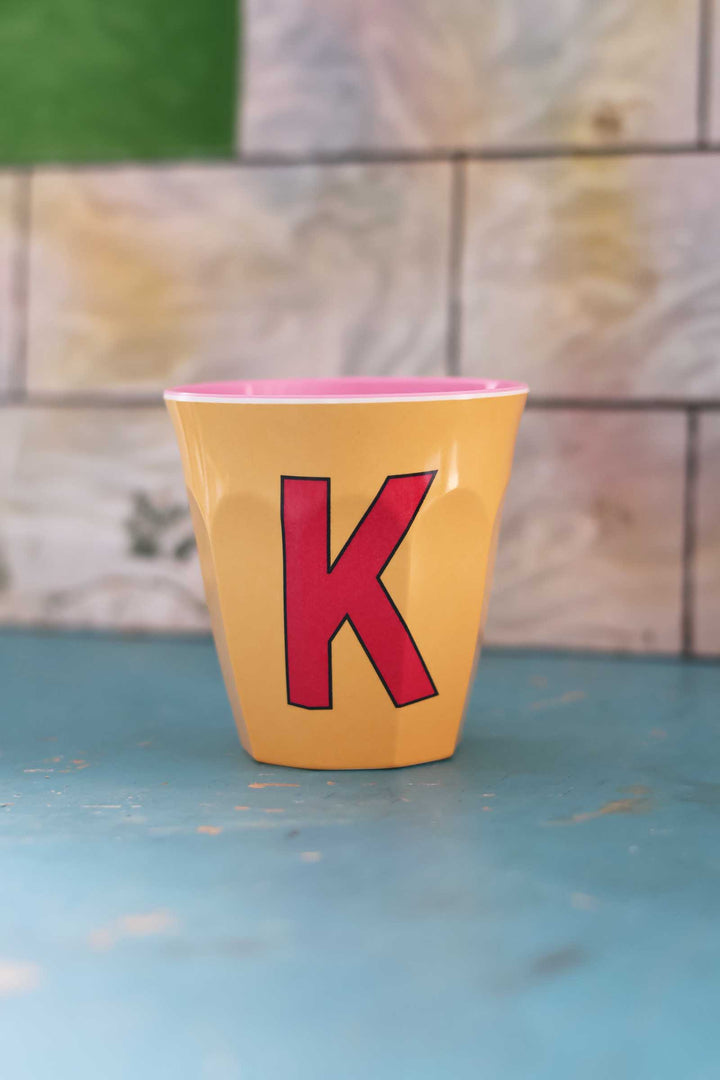 Yellow cup with a red letter 'K' on a blue surface with a blurred background