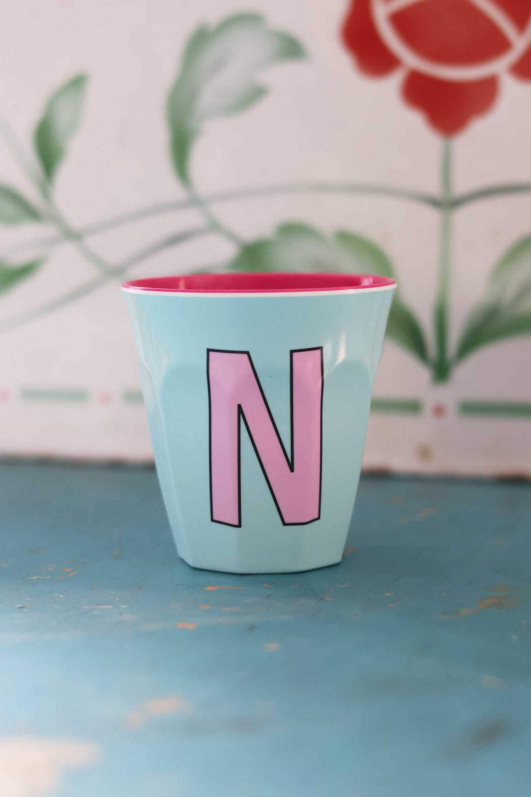 Light blue cup with pink interior and letter 'N' on a floral background