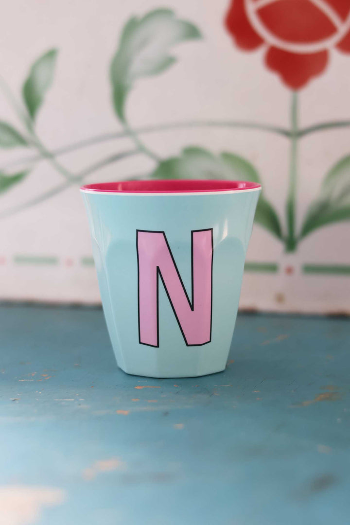 Light blue cup with pink interior and letter 'N' on a floral background
