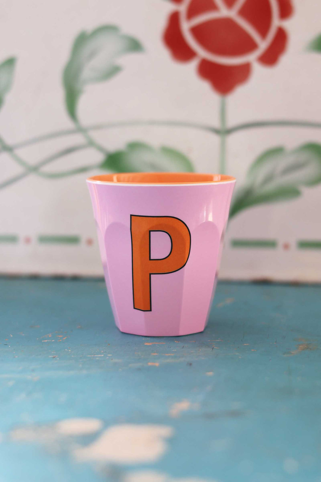 Pink cup with an orange letter 'P' on a blue surface with a floral background