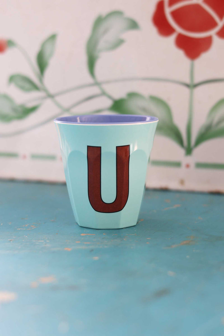 Teal cup with a brown letter 'U' on a blue surface with floral background