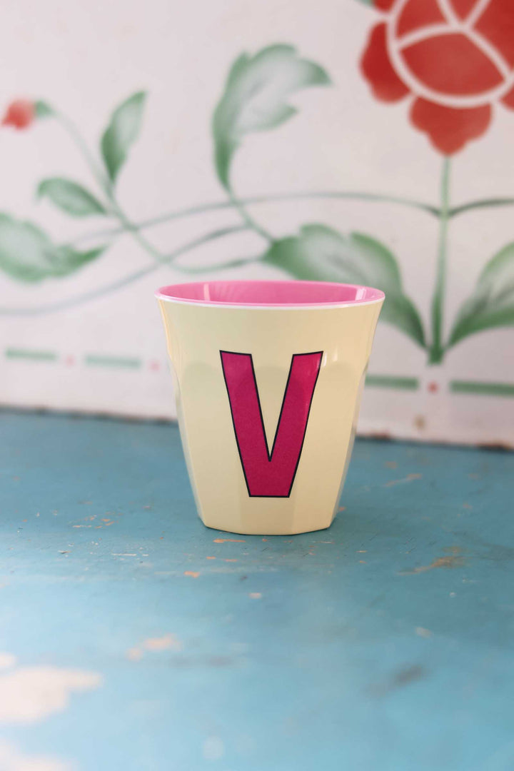Small pot with pink interior and letter 'V' on a blue surface with floral background