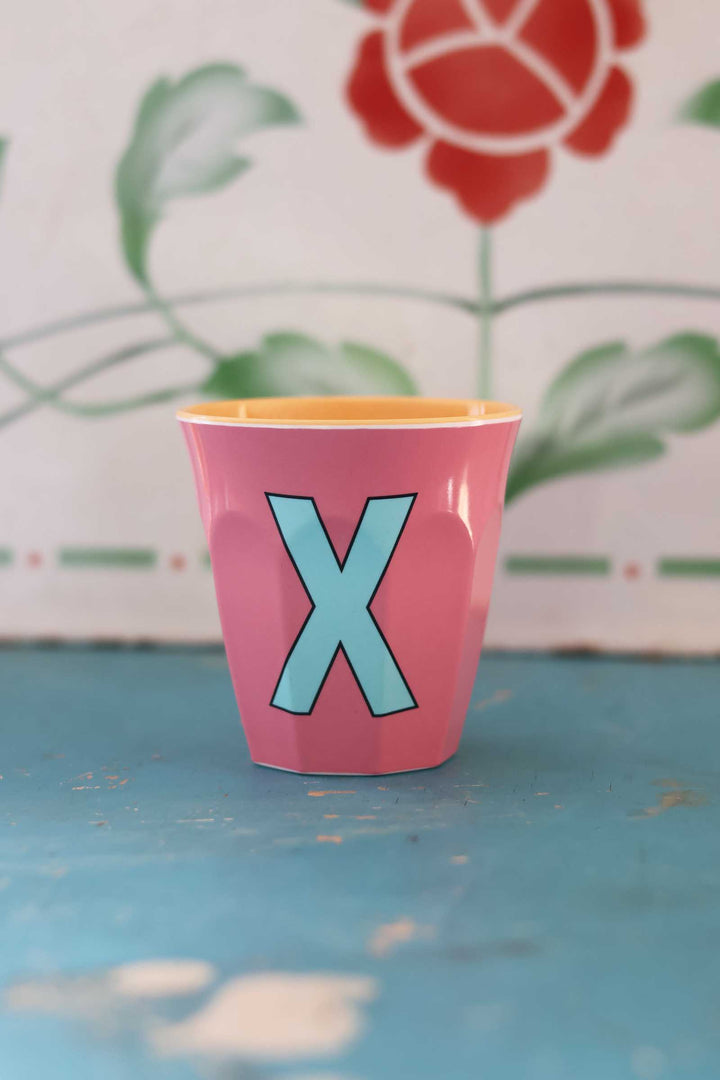 Pink cup with a blue 'X' on a blue surface with a floral background