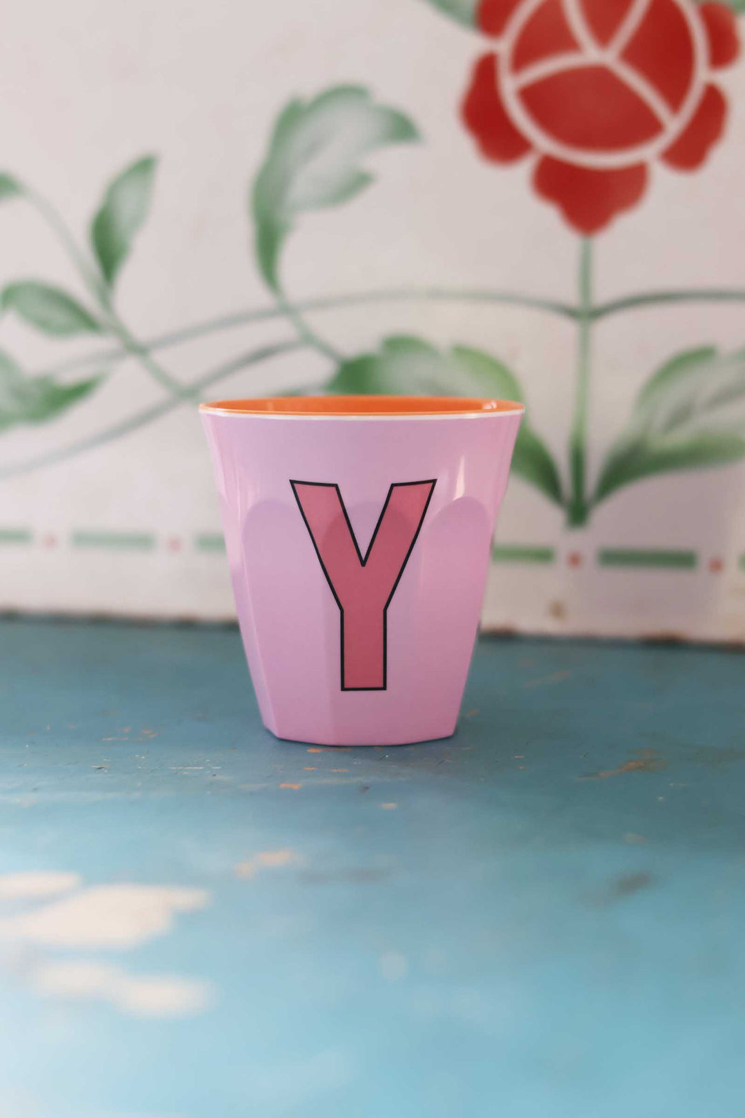 Pink cup with a red letter 'Y' on a blue surface with a floral background