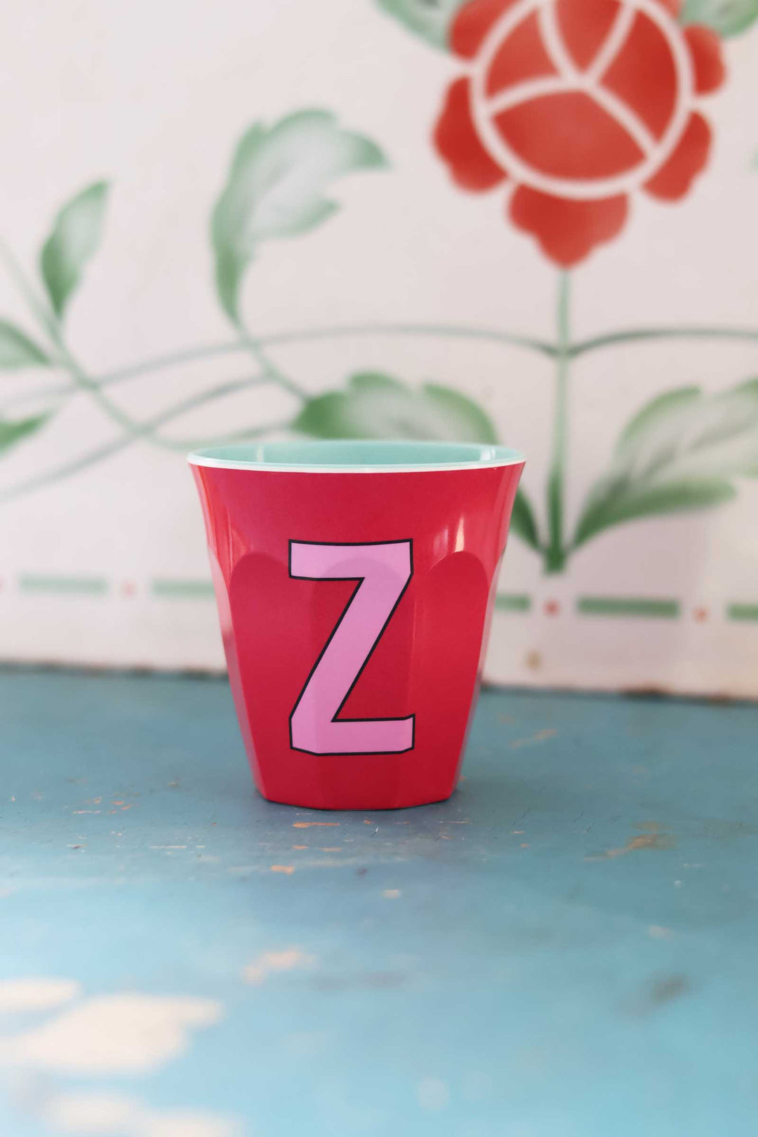 Red cup with a pink letter 'Z' on a blue surface with a floral background