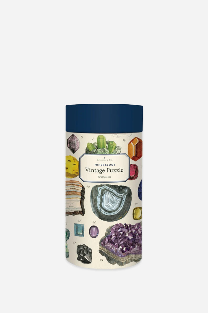 A vintage-style cylindrical puzzle tin with a dark blue lid and an illustrated label reading &