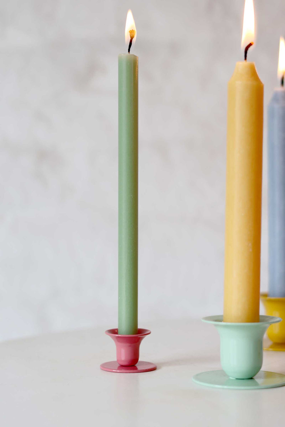 Three colorful candles in holders on a white surface with a light gray background