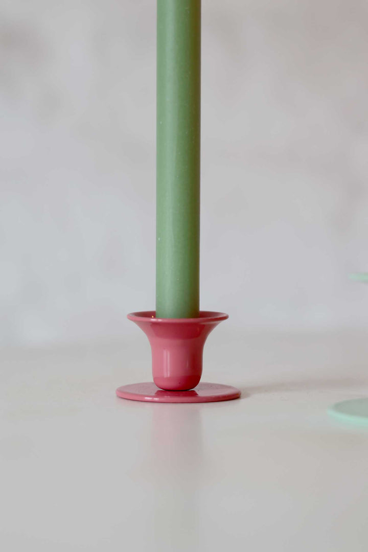 Green candle in a pink holder on a white surface with a light gray background
