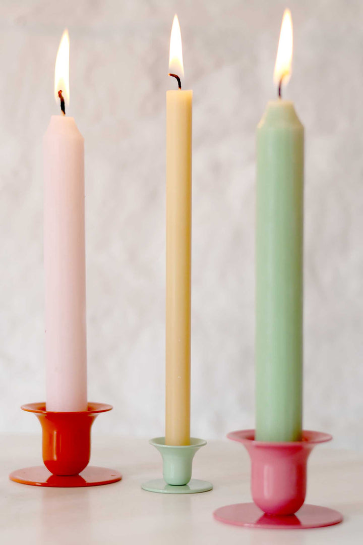 Three pastel-colored candles in colorful holders on a white background