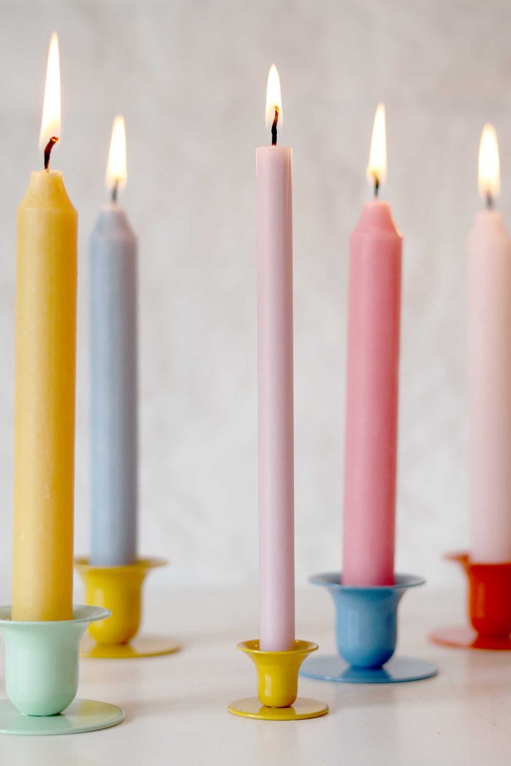 Colorful candles in various holders on a light background