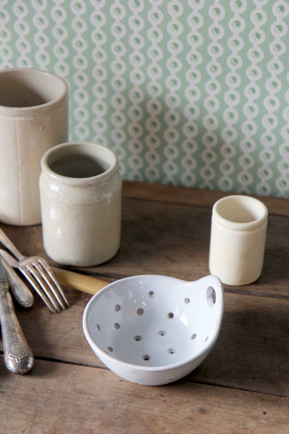 Set of ceramic bowls and cups on a wooden surface with a patterned wallpaper background.