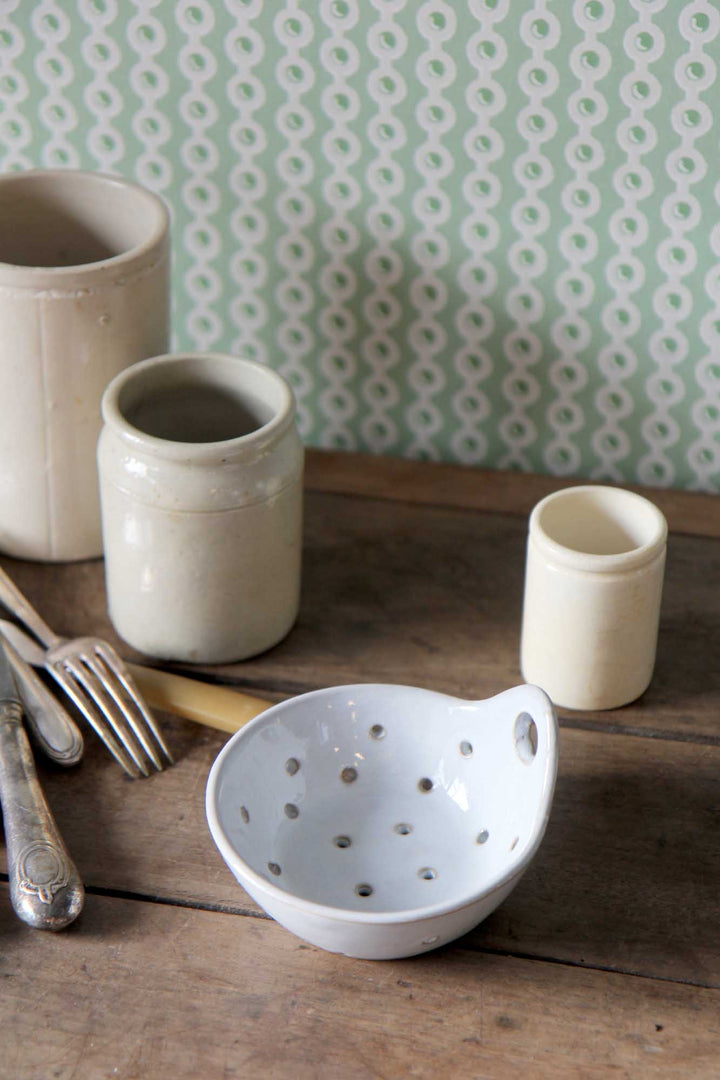 Set of ceramic bowls and cups on a wooden surface with a patterned wallpaper background.