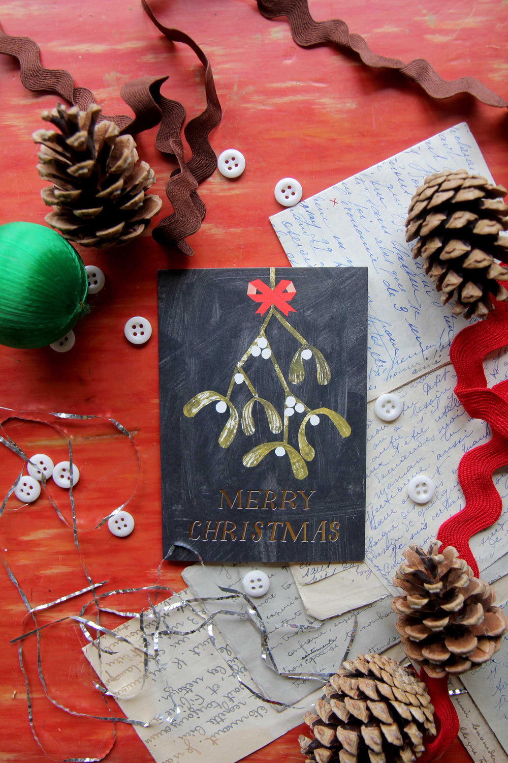 Christmas card with mistletoe design surrounded by festive decorations on a red surface.