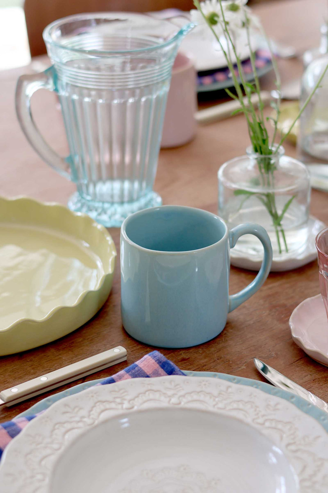 Dining table setting with a blue mug, green plate, and floral arrangement.