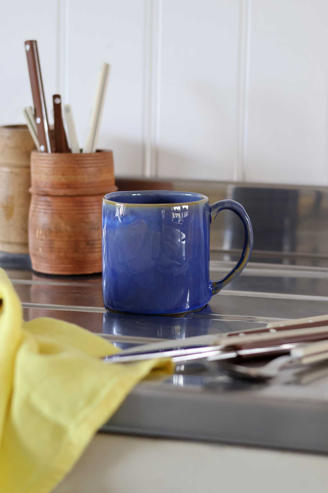 Blue mug on a kitchen counter with utensils and a yellow towel.