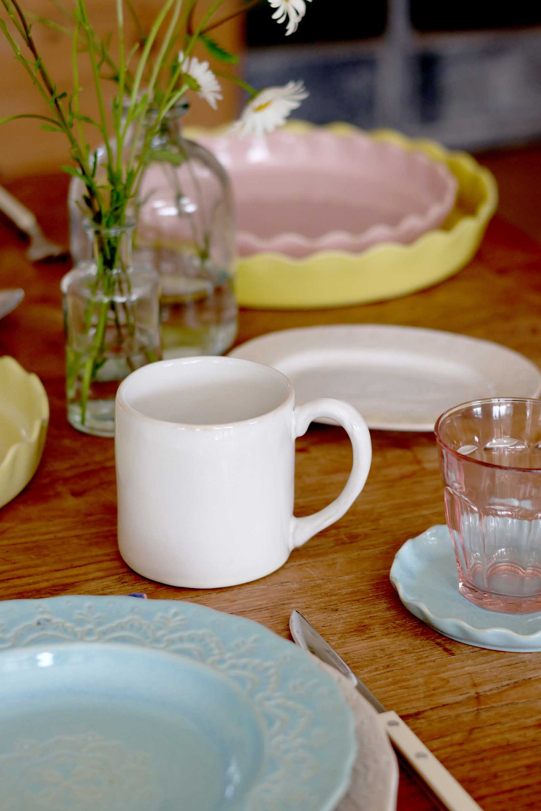 Dishes and tableware on a wooden table with a vase of flowers.