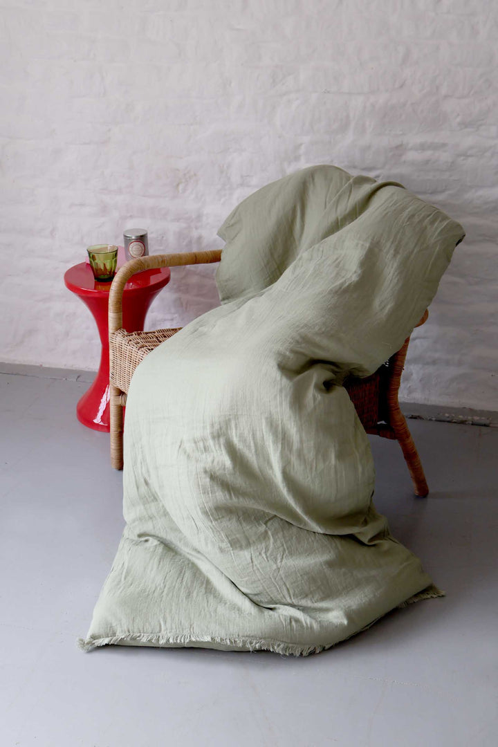 Light green fabric draped over a wicker chair against a white wall.