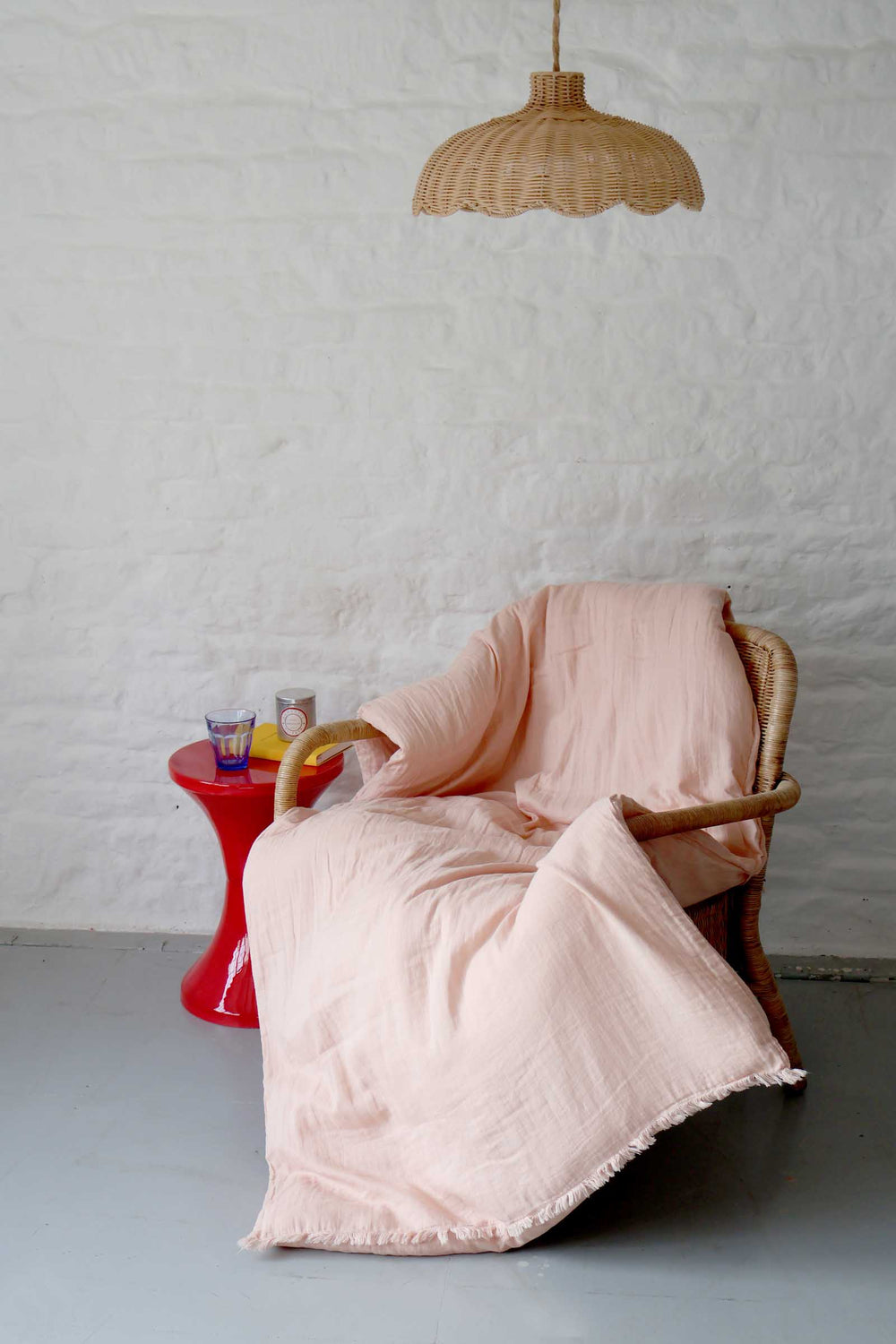 Pink blanket draped over a wicker chair with a red side table and hanging lamp in the background.