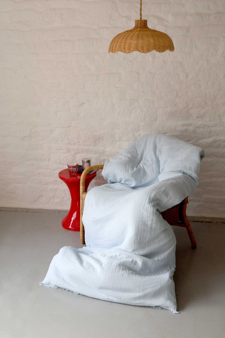 White draped fabric on a chair with a red side table and wicker lamp in a minimalistic room.