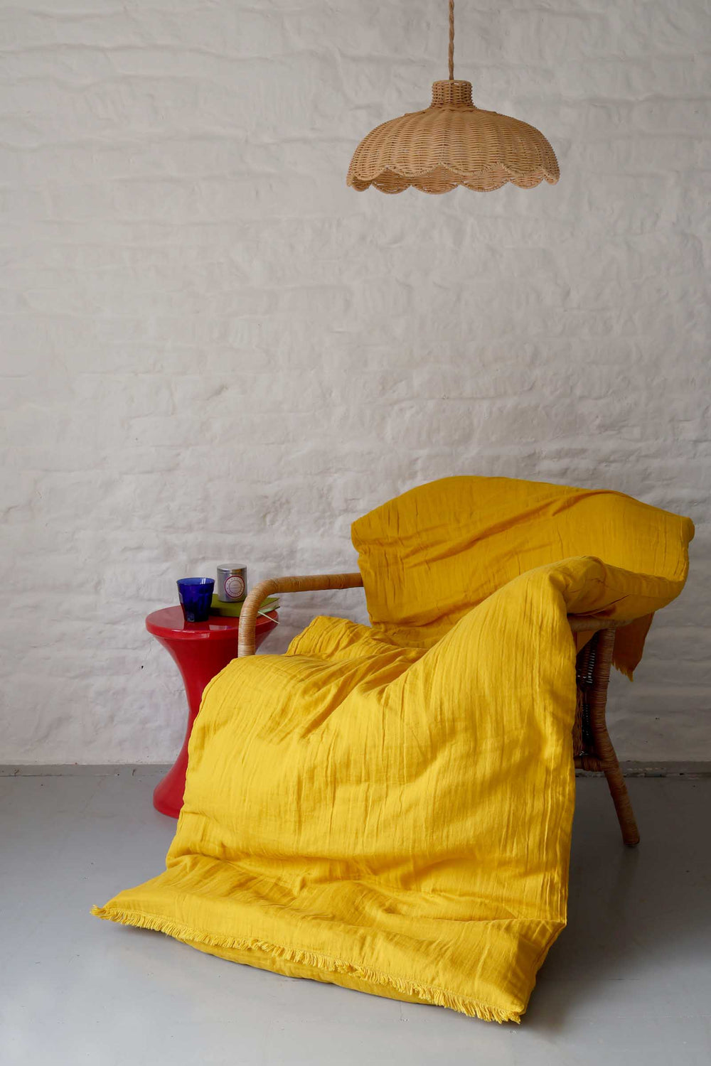 Yellow blanket draped over a chair in a room with a textured white wall and a red stool.