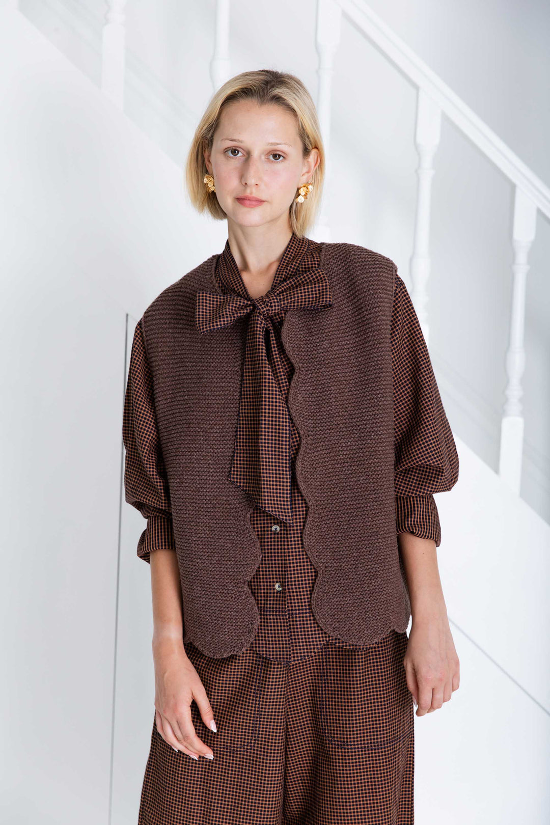 Woman wearing a brown checkered outfit with a bow tie against a white background