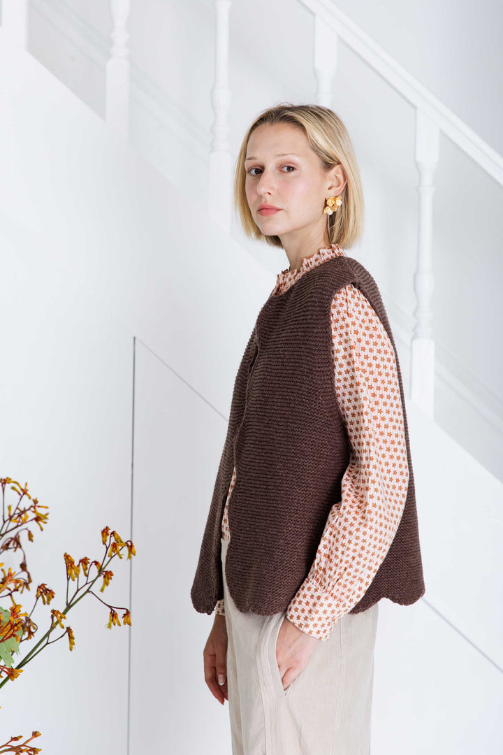 Woman wearing a brown knitted vest over a patterned shirt against a white background