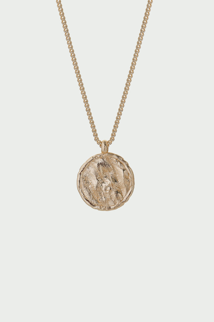 Gold necklace with a round pendant on a light gray background