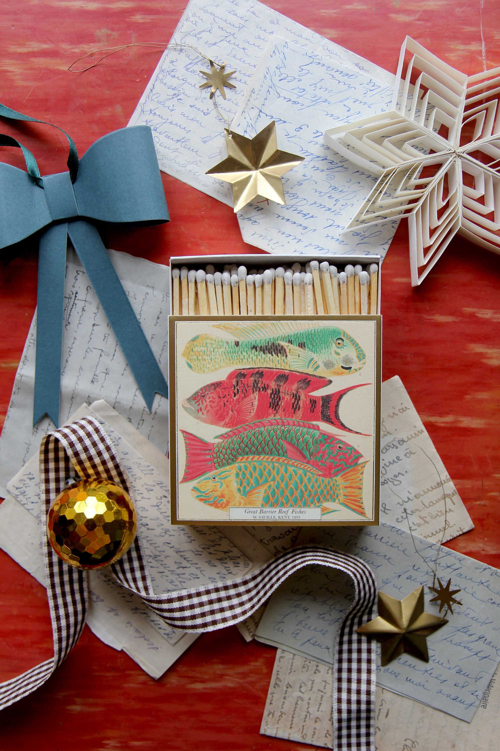 Matchbox with fish design on a decorative surface with ribbons and stars.