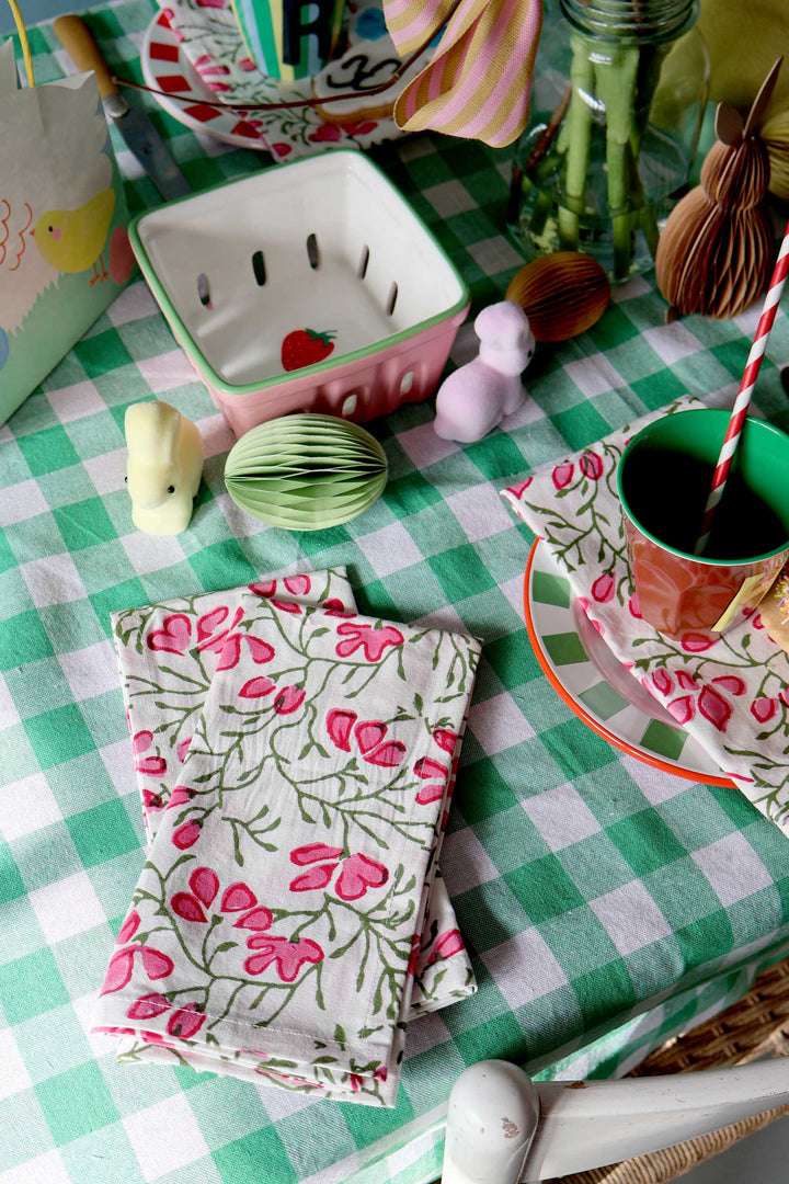 Children's table setting with floral napkins, cups, and checkered tablecloth.