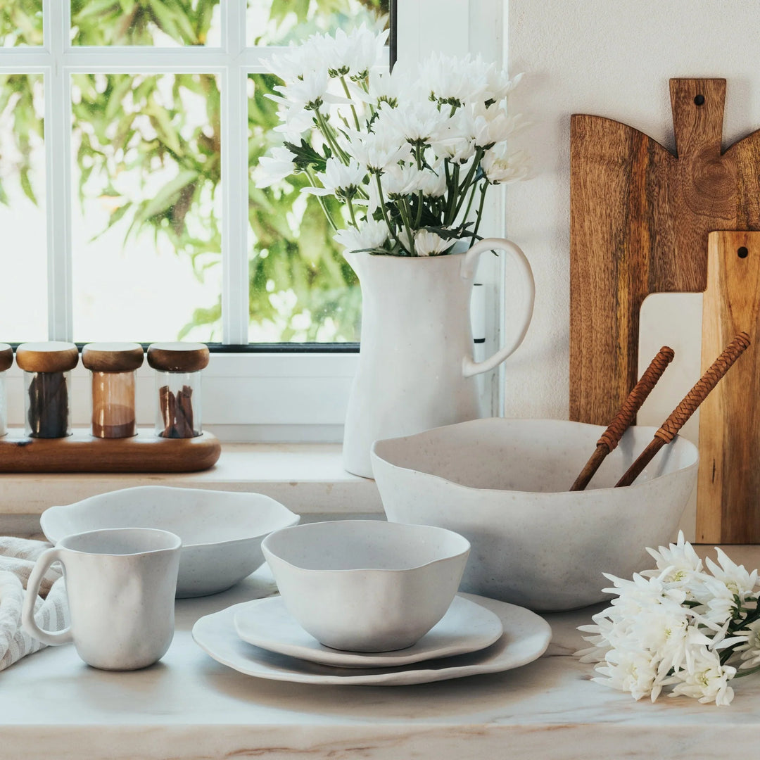 White ceramic dishes on a table with wooden cutting boards and flowers in the background.